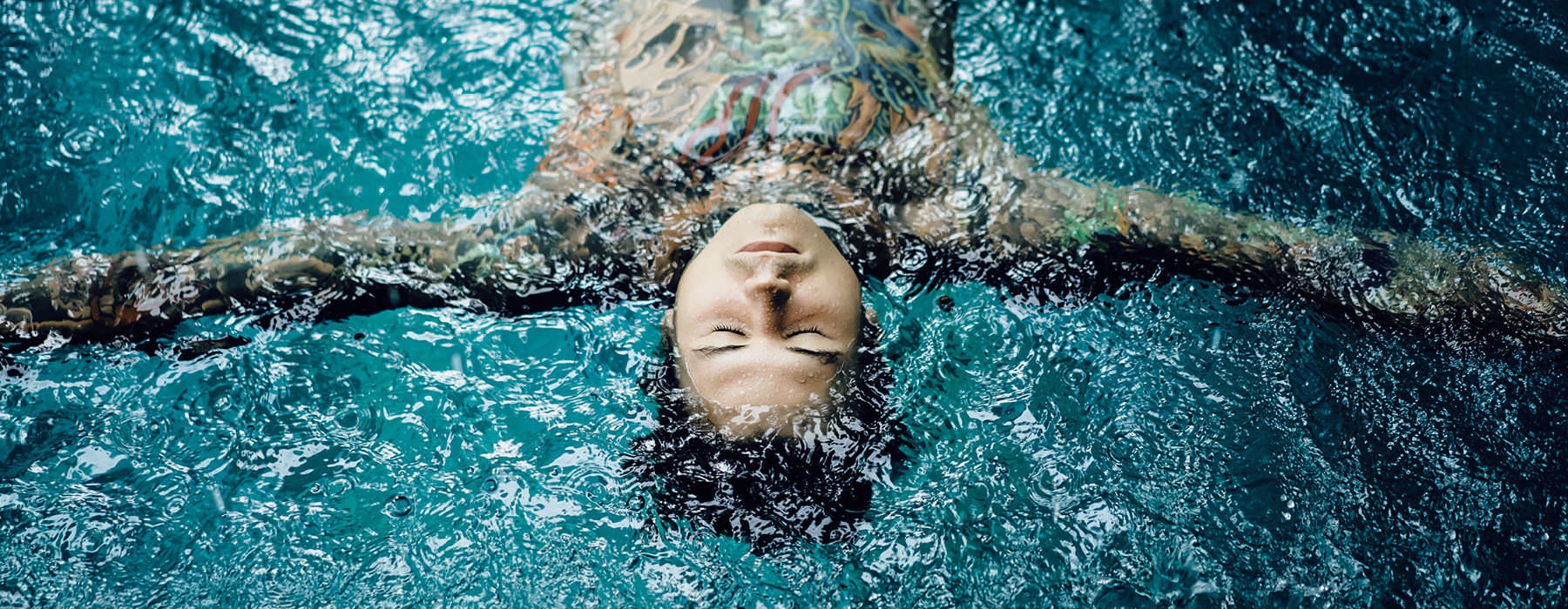 tattooed man floats on his back and relaxes in pool