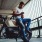 scruffy guy with a white tee and torn jeans lean against his motorcycle in parking garage as he looks at his phone