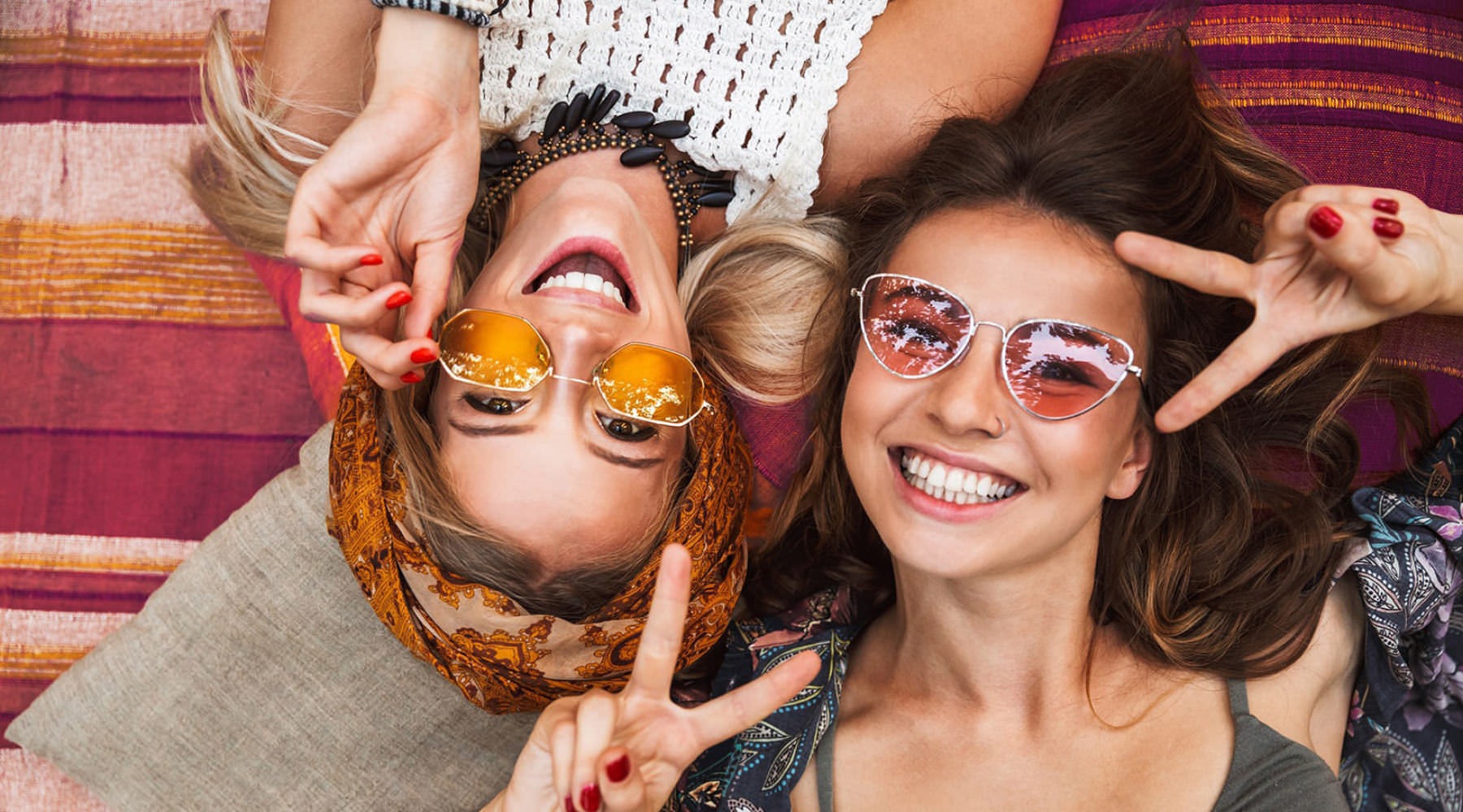 overhead view of two girls in bohemian dress as they lay on cushions and smile at the camera